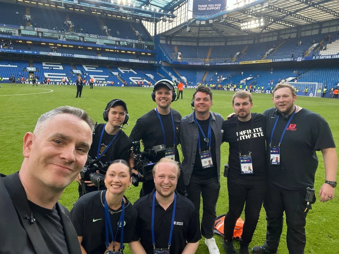 A broadcast team standing together on the pitch at Stamford Bridge
